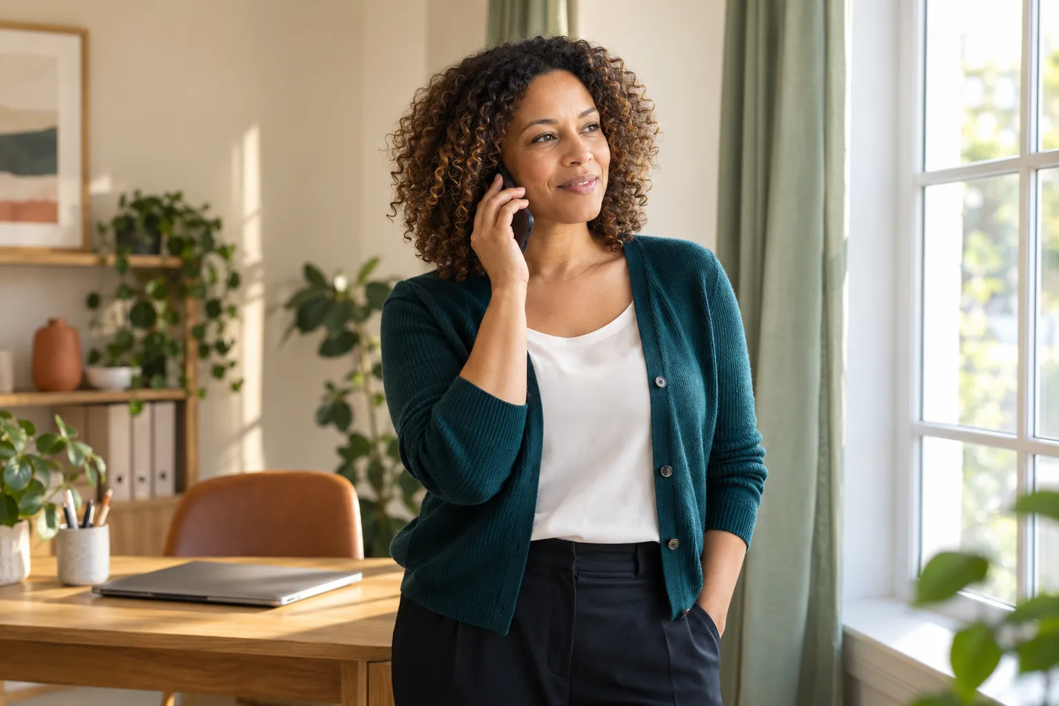 Business owner having a phone conversation beside a bright office window.